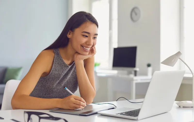 A smiling woman taking notes beside a laptop